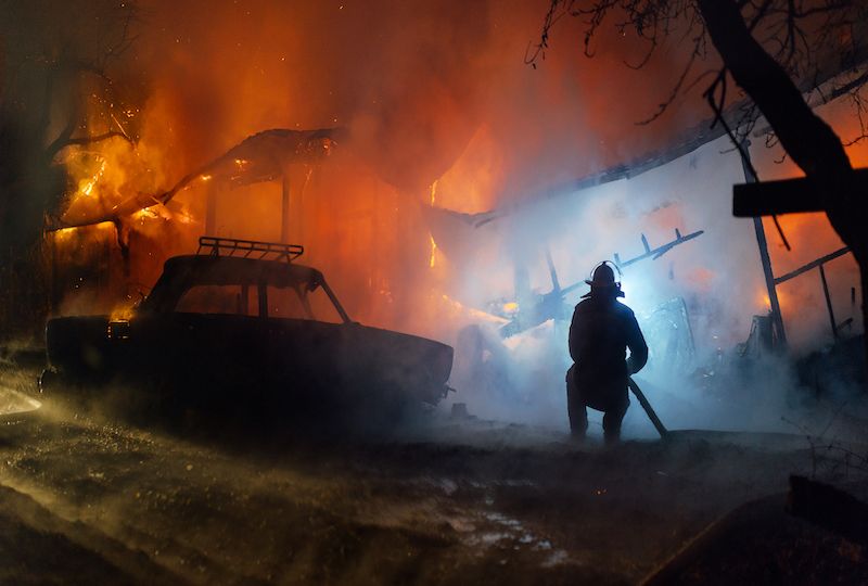 Firefighter putting out the fire of the house and car