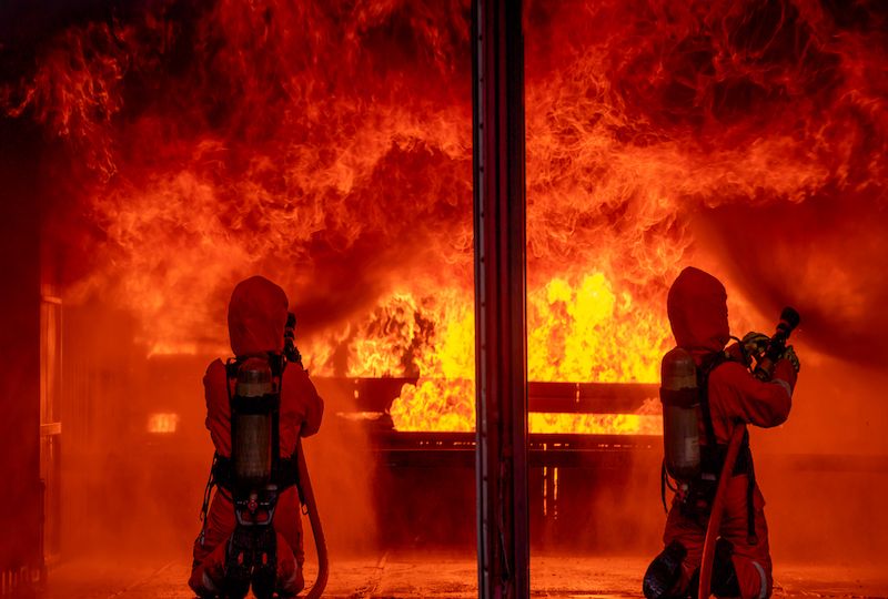 Two firefighters spray water by sprinkler to extinguish or get rid huge fire in room that cover by fire  and smoke.