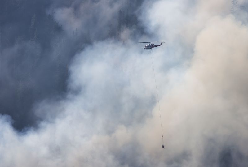 Wildfire Service Helicopter flying over BC Forest Fire and Smoke on the mountain near Hope